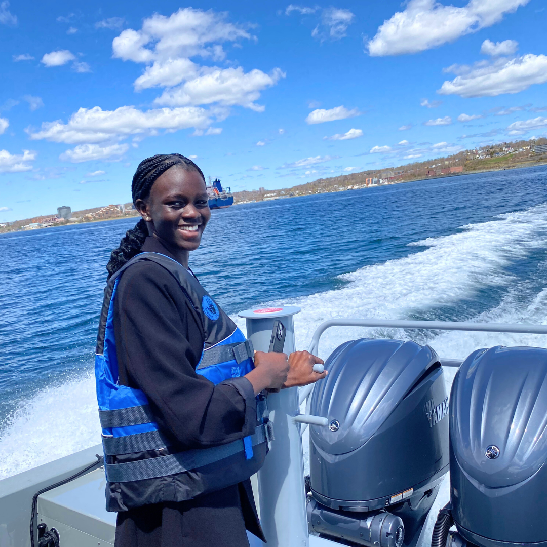 Mary smiles, wearing a life jacket on a boat. with the ocean behind her.