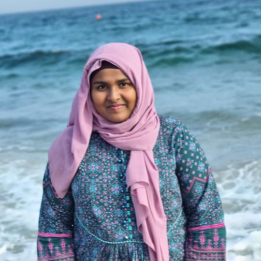 Hira stands and smiles with ocean waves behind her.