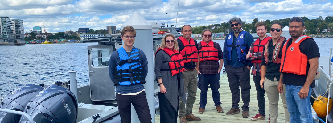 A group of SEATAC and Marecomms staff pose for a photo with the research vessel on COVE's floating docks.